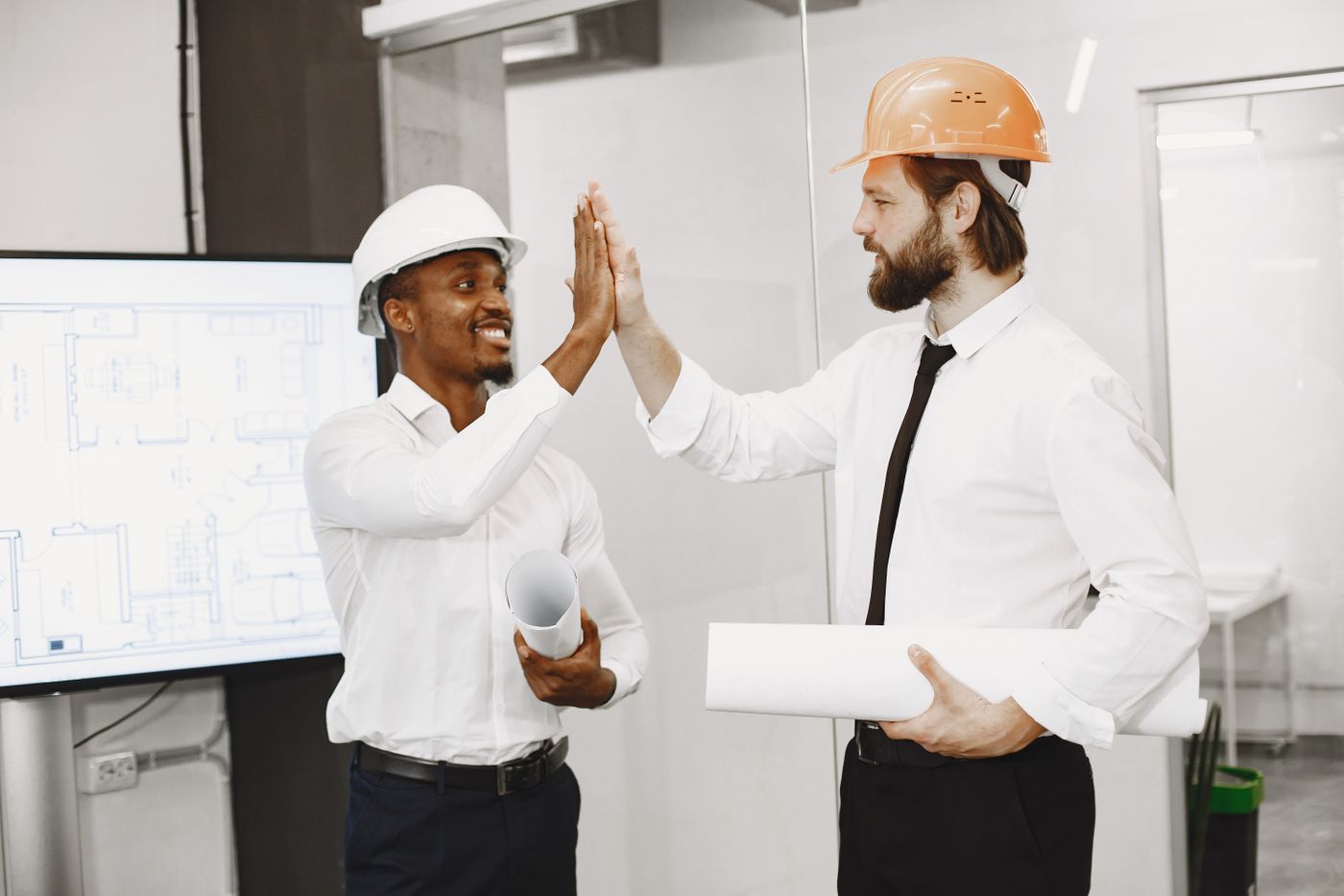 Two young coworkers in hard hats sharing a high five